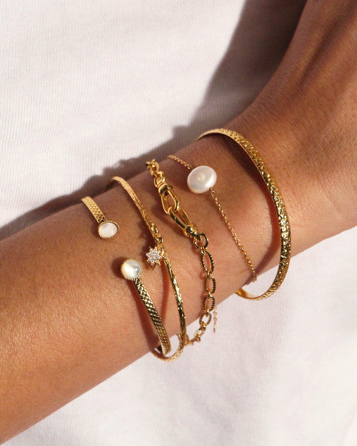 Femme au t-shirt blanc portant des bracelets de la marque Nilaï. Elle porte un jonc simple, un jonc orné d'une étoile polaire, un jonc orné d'une pierre nacrée et un bracelet orné d'une perle blanche