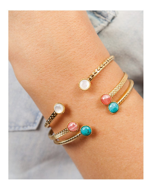 femme portant des bijoux nilai à son poignet. elle porte 3 jonc athéna, un est orné de quartz rose, le deuxième d'une nacre et le troisième d'une pierre turquoise