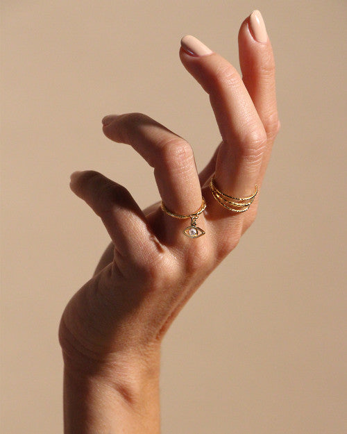 Main avec vernis nude sur les ongles portant deux bagues nilai : une avec un petit oeil, une autre fine et minimaliste