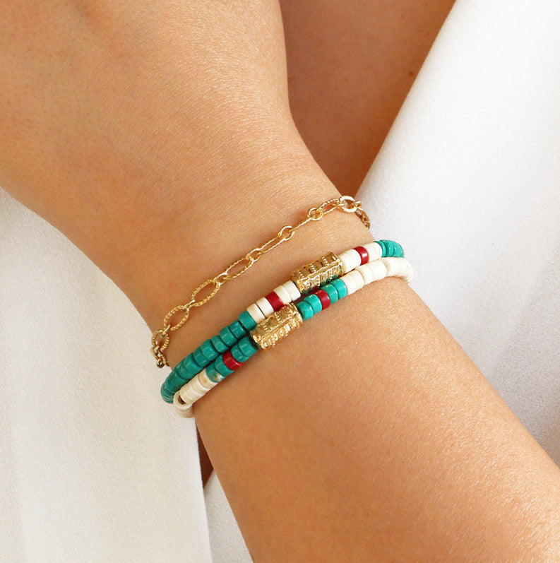 poignet portant des bracelets surfeurs à perles beiges et turquoises ainsi qu'un bracelet à maille pure torsadée