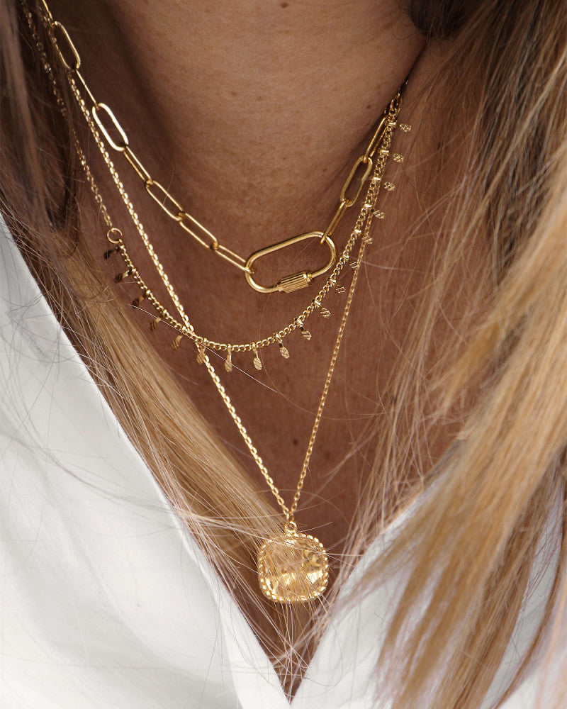 femme blonde portant des bijoux nilai : le collier lock, le collier fin alegria et le collier à médaille carrée sally