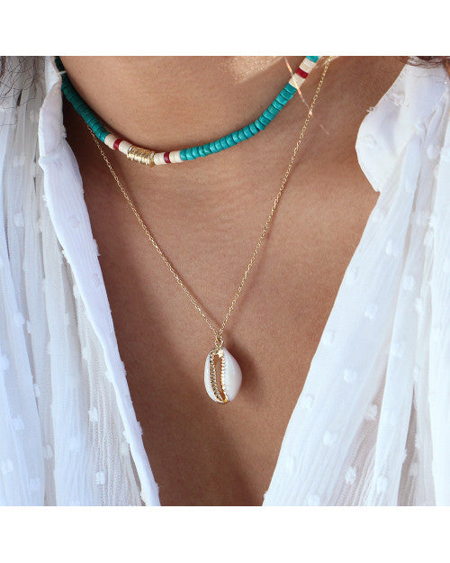 femme portant un collier surfeur à perles turquoises et un collier composé d'un coquillage cauri blanc